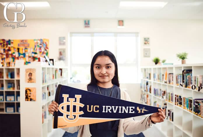 Elvira proudly holds a UC Irvine pennant in the KIPP Adelante library