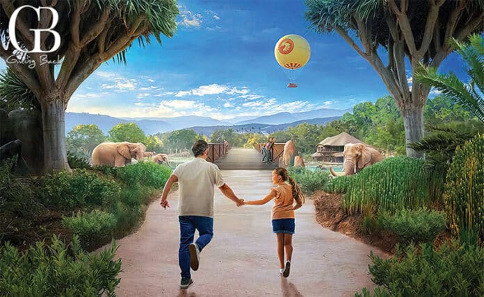 Two kids running hand-in-hand down a zoo path toward elephants in a lush tropical landscape with a hot air balloon in the sky.
