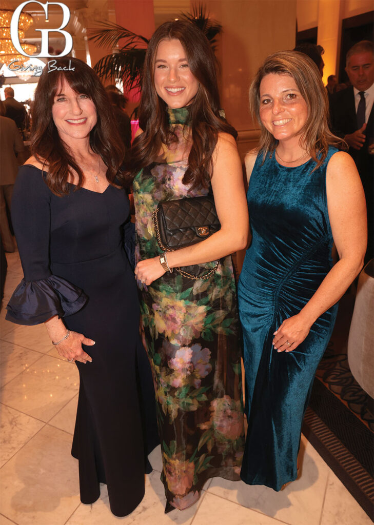 Gayle-McMahon-Meghan-Domingo-and-Lori-Schleicher - GB Magazine Gayle McMahon Meghan Domingo and Lori Schleicher'Giving Back' logo in the background.