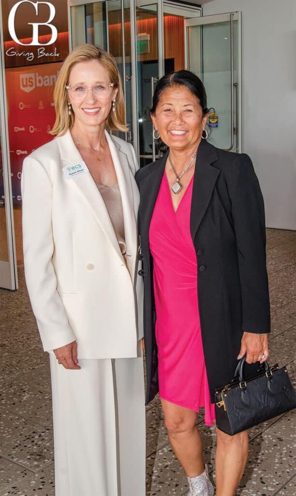 Elizabeth-Wilberg-and-Nancy-Sasaki - GB Magazine Elizabeth Wilberg and Nancy Sasaki'Giving Back' sign in the background.